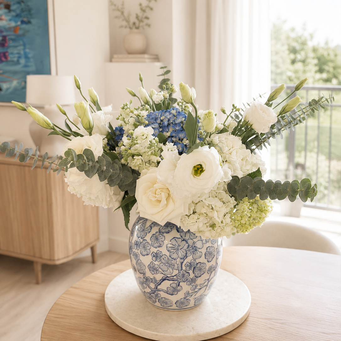 A blue and white patterned ceramic vase filled with a white and blue floral arrangement.