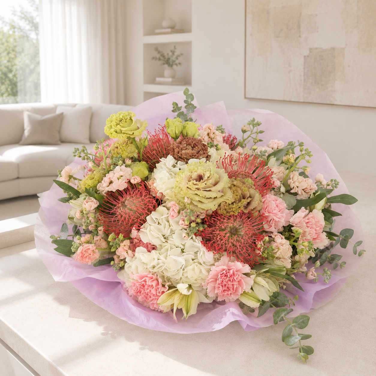 A large, vibrant floral bouquet wrapped in light purple tissue paper, displayed on a white table in a bright, modern living room setting.